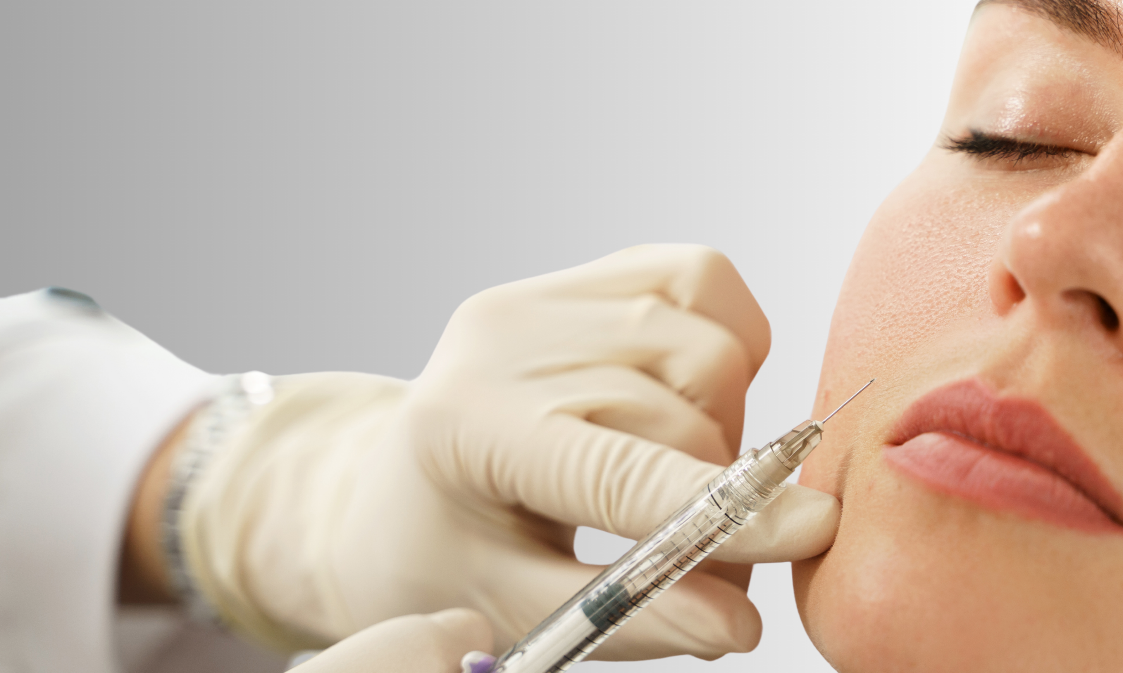 Person receiving a facial injection with a syringe held by a gloved hand.