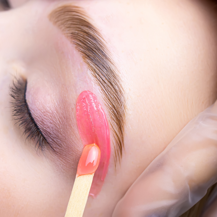 Eyebrow waxing process with a strip and matchstick on a blurred background