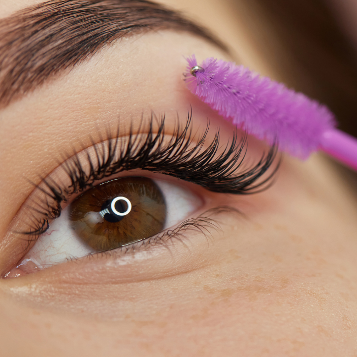 Close-up of an eye with false eyelashes being applied using a purple applicator.