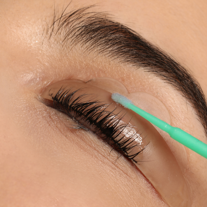 Eyelash extension application with a green tool on a close-up of an eye.